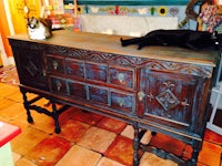 a black cat is laying on top of a wooden sideboard in a kitchen